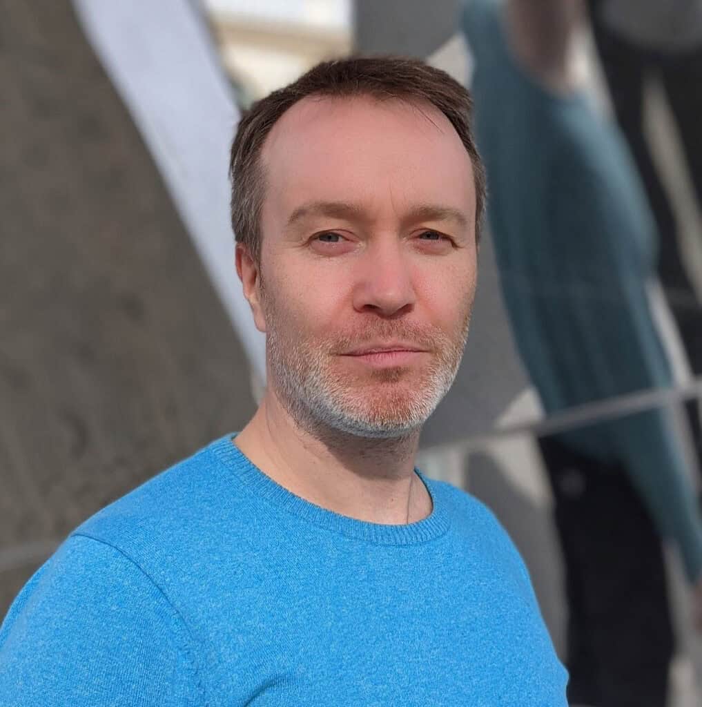 Oliver Atherton's headshot in blue shirt